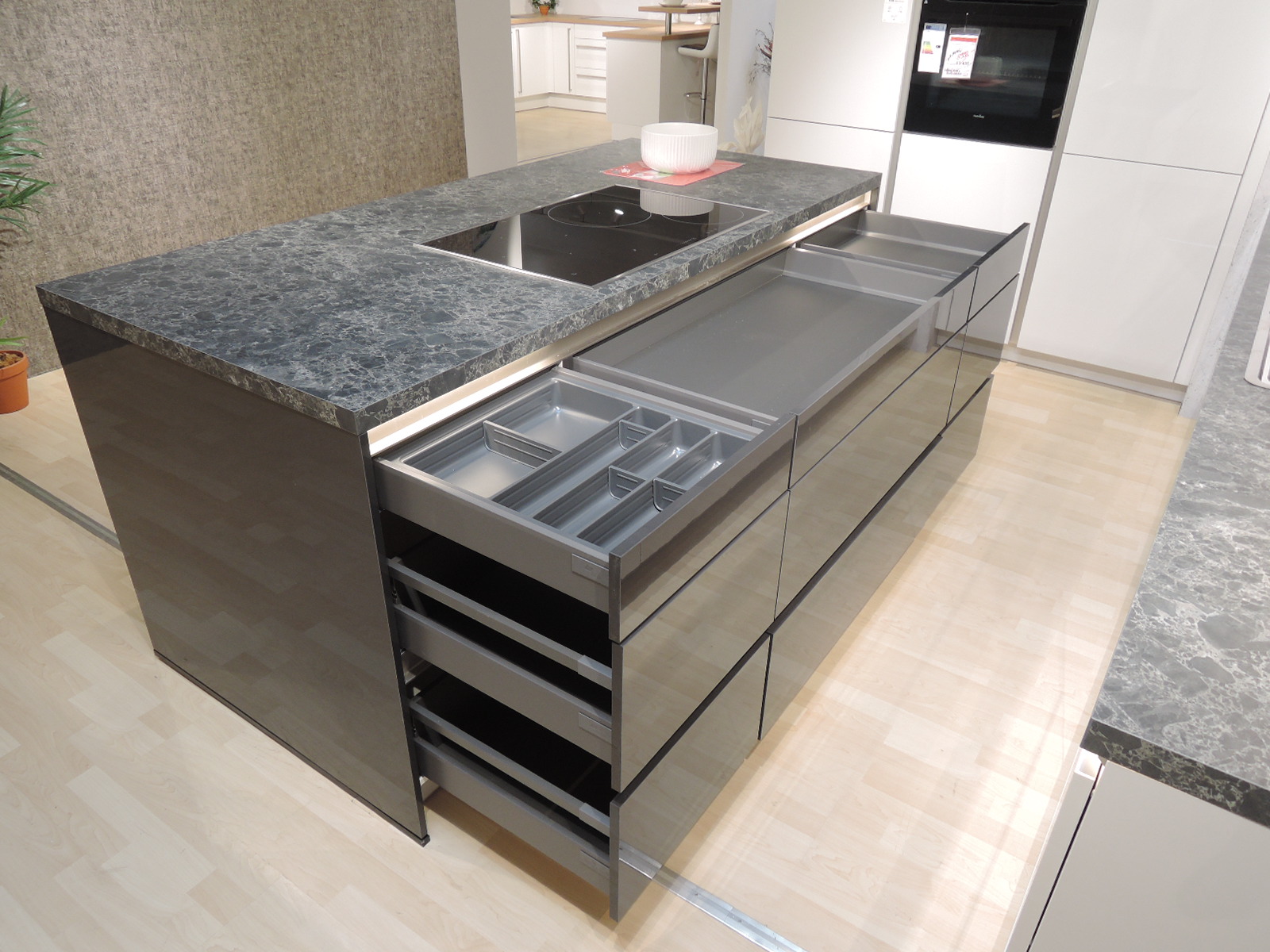 Direktansicht auf die Vorderseite der Kochinsel mit geöffneten Schubladen mit Besteckeinsatz und geöffneten Auszügen
