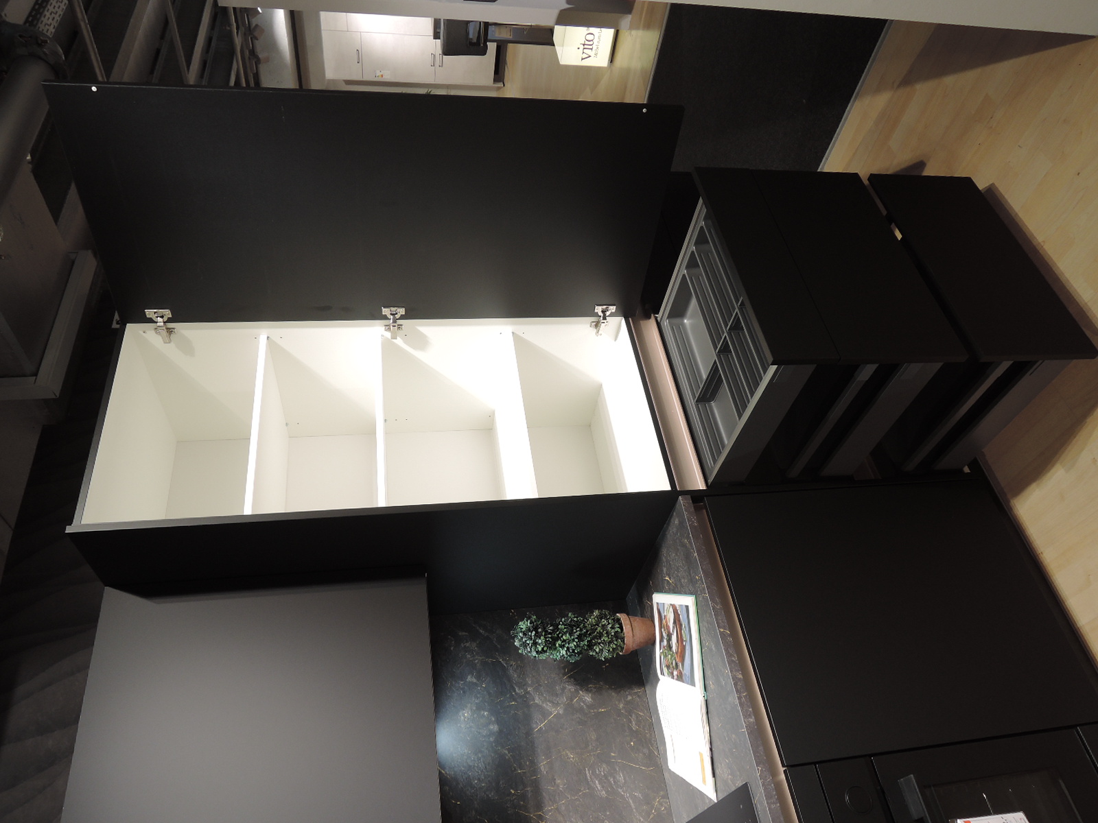 Blick in den geöffneten Schrank links vom Kühlschrank  mit darunterliegenden geöffneten Auszügen und Schublade mit Besteckeinsatz