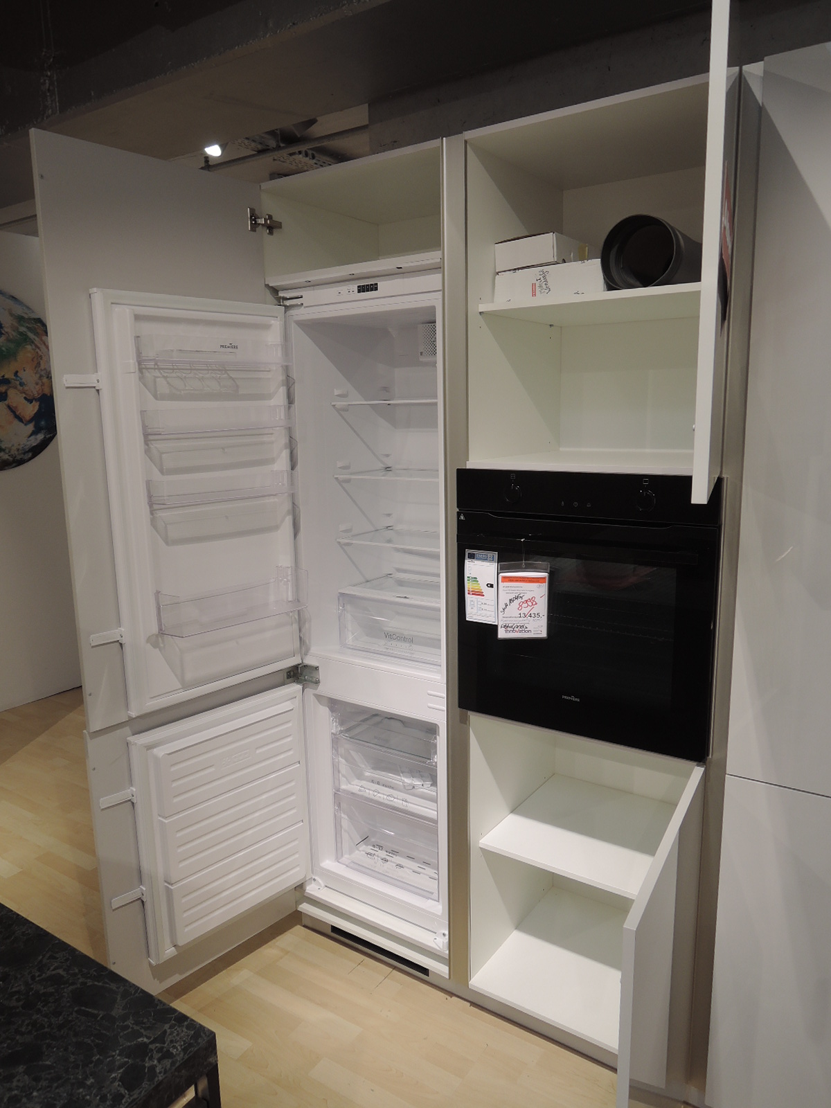 Blick in die geöffnete Kühl-Gefrierkombination und in die geöffneten Schränke oberhalb und unterhalb des Backofens