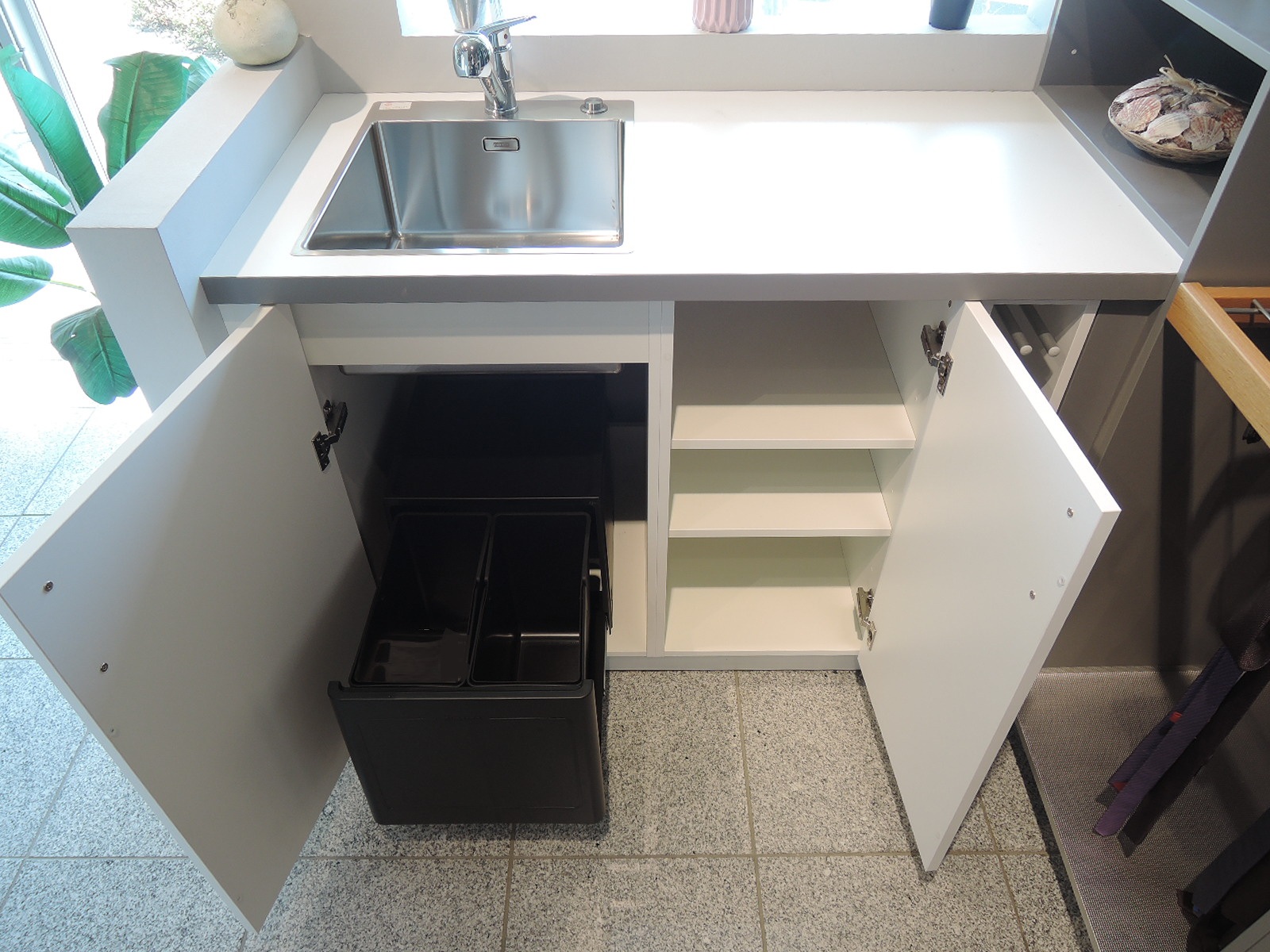 Blick in den geöffneten Spülenunterschrank mit Abfallsammler der Marke Blanco sowie der Einbauspüle mit Armatur der Marke Franke des Hauswirtschaftsraumes im Abverkauf Novel der Marke Interleine