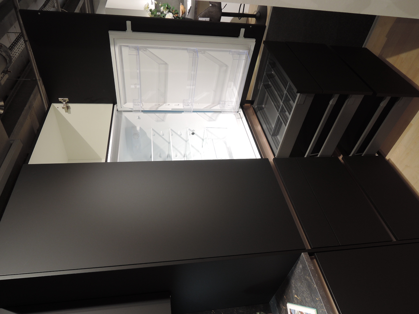 Blick in den geöffneten Kühlschrank mit darunterliegenden geöffneten Auszügen und Schublade mit Besteckeinsatz