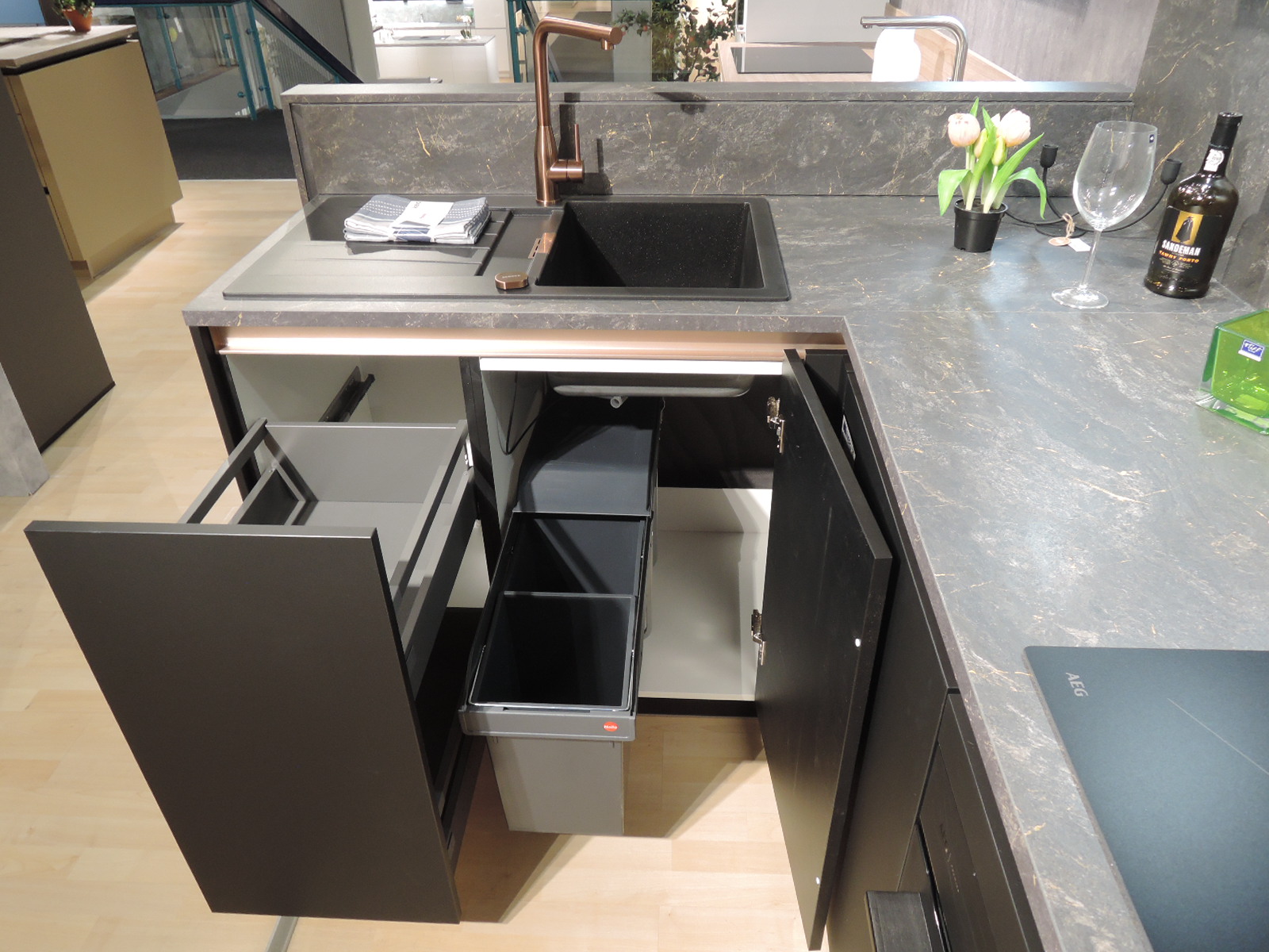Blick in den geöffneten Auszugunterschrank links vom Spülenunterschrank und in den geöffneten Spülenunterschrank mit Müllsystem